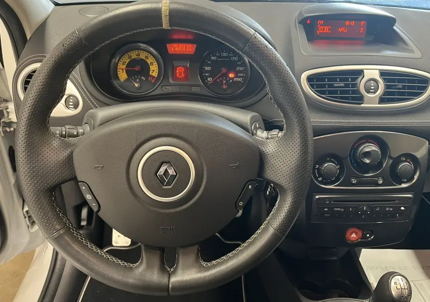Vue intérieure centrée sur le volant en cuir noir perforé et le tableau de bord de la Renault Clio III RS 20th Anniversary.