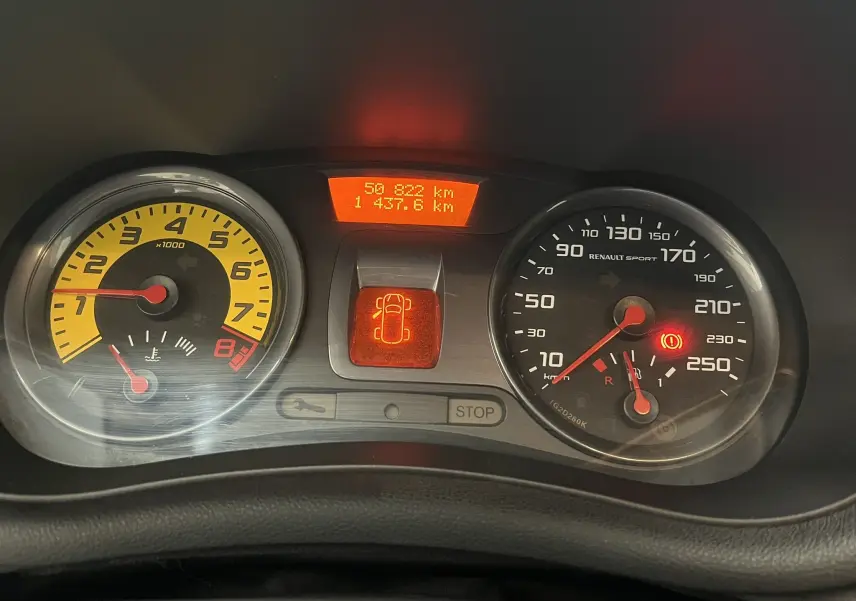 Gros plan sur le tableau de bord de la Renault Clio III RS 20th Anniversary avec compte-tours jaune et affichage digital orange.