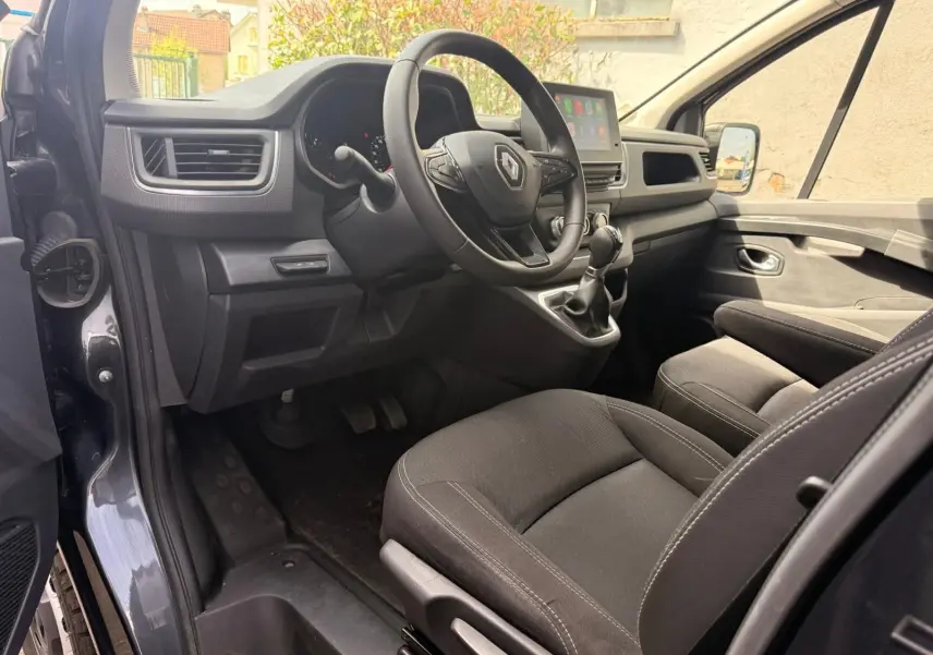 Vue intérieure côté conducteur du Renault Trafic gris comète, montrant le volant multifonction et la console centrale avec écran tactile.