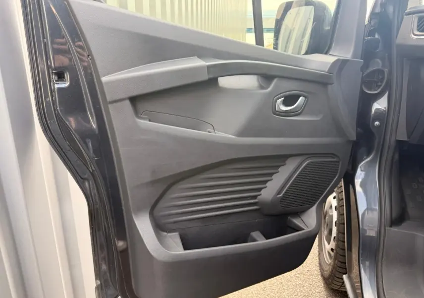 Vue rapprochée de la porte latérale gauche ouverte du Renault Trafic gris comète, montrant les rangements et la poignée intérieure.
