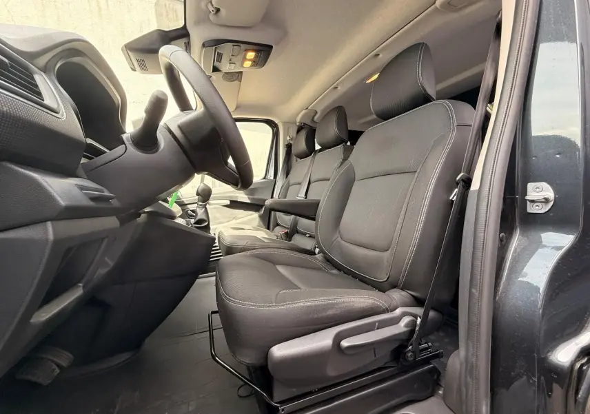 Vue intérieure côté conducteur du Renault Trafic gris comète 2024, montrant les sièges avant en tissu noir et le volant.