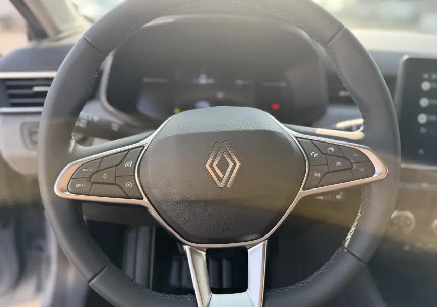 Vue rapprochée du volant noir de la Renault Clio 1.5 DCI 2025 avec commandes intégrées et logo central chromé.