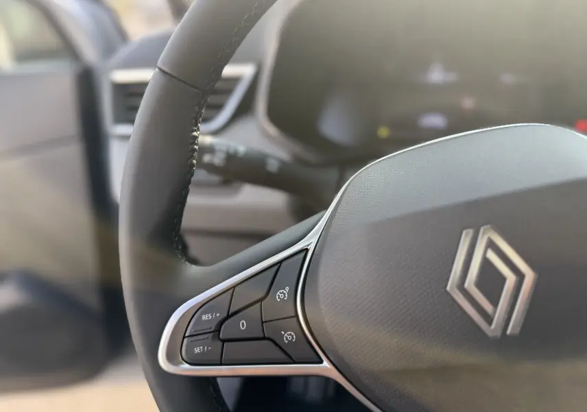 Gros plan sur le volant noir de la Renault Clio 2025 avec commandes intégrées et logo au centre.