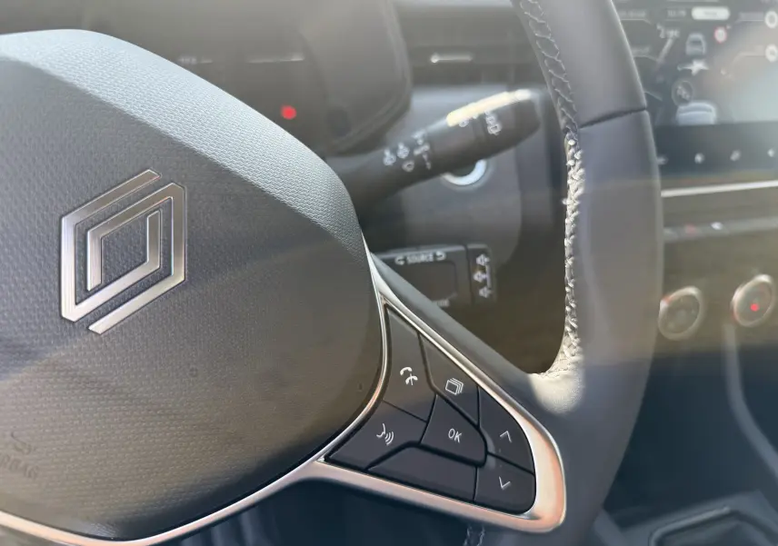 Gros plan sur le volant noir de la Renault Clio 2025 avec commandes intégrées et logo stylisé au centre.
