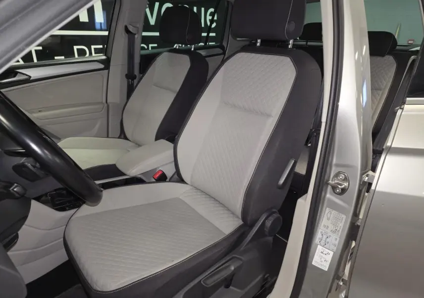 Vue intérieure côté conducteur du Volkswagen Tiguan 2018, sièges tissu gris clair avec accoudoir central.