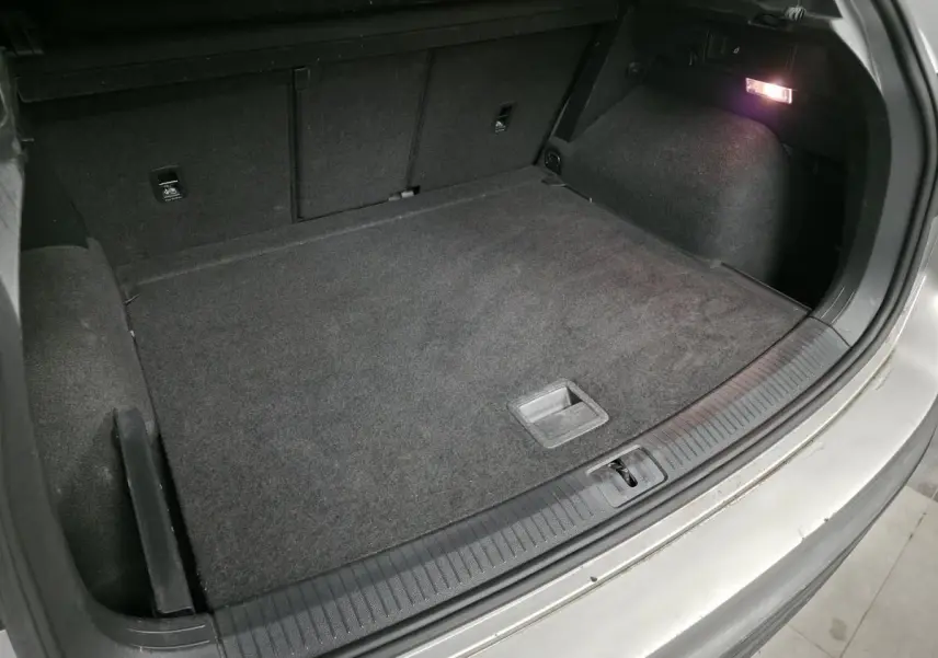 Coffre ouvert du Volkswagen Tiguan gris, vue plongeante montrant l'espace de chargement et l'éclairage intérieur.