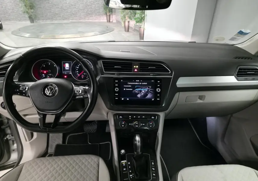Vue intérieure avant du Volkswagen Tiguan gris, tableau de bord avec écran tactile et volant multifonctions cuir.