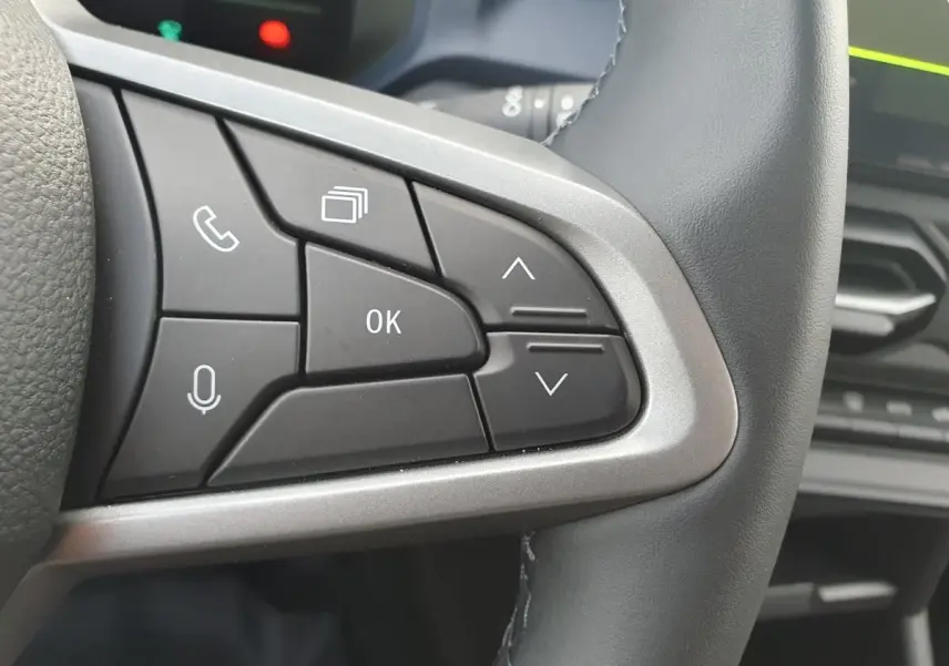 Gros plan sur les commandes multifonctions à droite du volant du Dacia Duster 1.6 Hybrid 140 gris schiste, intérieur moderne.