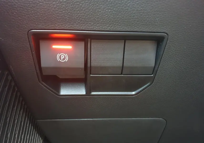 Gros plan sur le bouton de frein de stationnement électrique allumé, intérieur noir du Dacia Duster 1.6 Hybrid 2026.