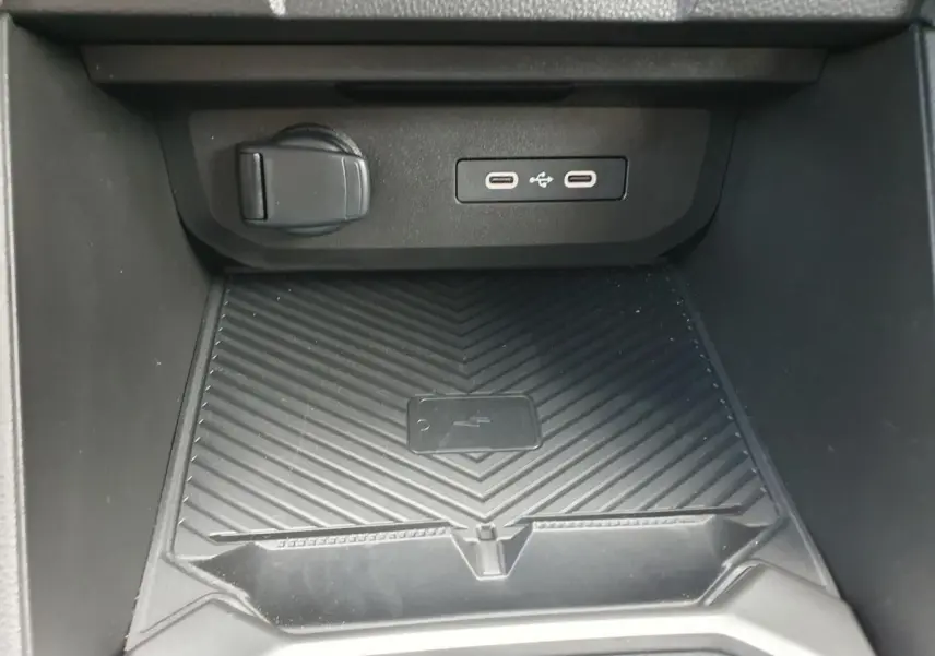 Vue rapprochée de la console centrale du Dacia Duster 2026 montrant la zone de charge sans fil et ports USB.