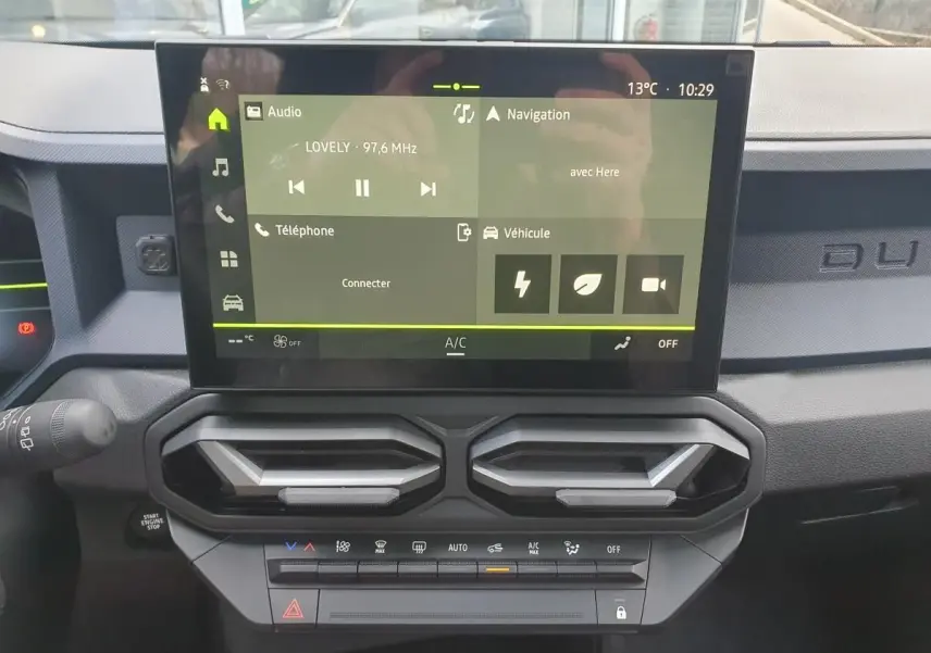 Vue rapprochée du tableau de bord du Dacia Duster 2026, écran tactile central avec commandes climatisation et aérateurs noirs.