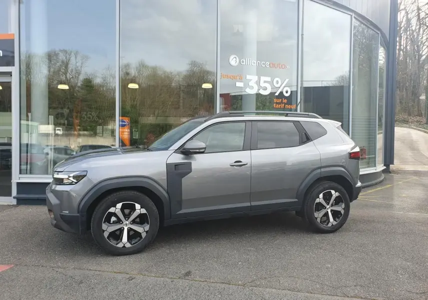 Vue de profil côté gauche du Dacia Duster gris schiste 2026 avec jantes alliage 18 pouces et barres de toit noires.