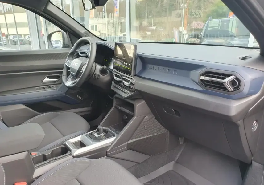 Vue intérieure côté conducteur du Dacia Duster 2026 gris schiste, tableau de bord moderne avec écran tactile central.