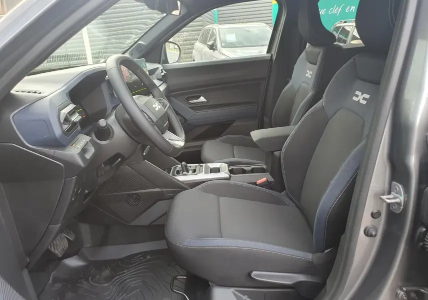 Vue intérieure côté conducteur du Dacia Duster 2026 gris schiste, sièges tissu avec logo et tableau de bord moderne.