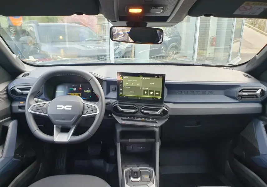 Vue intérieure avant du Dacia Duster 1.6 Hybrid 140 gris schiste, tableau de bord moderne avec écran tactile central.