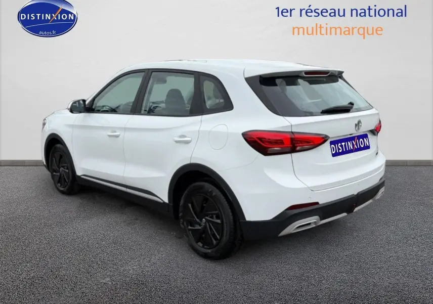 Vue 3/4 arrière droite d'un MG ZS Hybrid blanc avec jantes noires et feux arrière LED sur fond neutre.