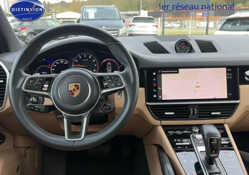 Vue intérieure avant du tableau de bord beige et volant cuir noir du Porsche Cayenne hybride avec écran tactile et levier de vitesse.