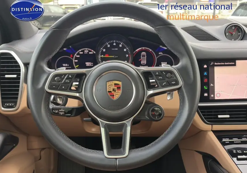 Vue intérieure centrée sur le volant cuir noir et tableau de bord beige du Porsche Cayenne hybride 2023.