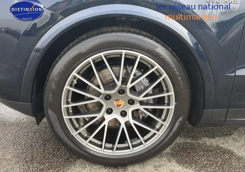 Gros plan sur la roue avant droite d’un Porsche Cayenne bleu avec jante alu multibranches et logo Porsche au centre.