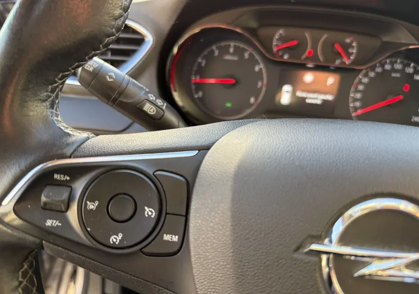 Gros plan sur le volant noir de l'Opel Grandland X 2019 avec commandes intégrées et tableau de bord flou en arrière-plan.