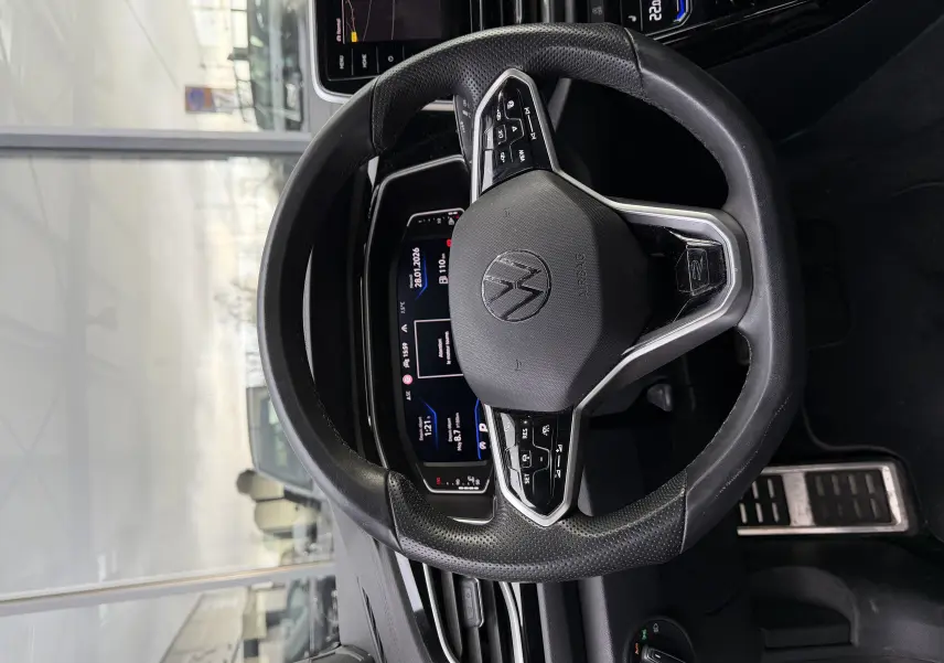 Vue rapprochée du volant multifonction noir du Volkswagen T-Roc Cabriolet blanc, avec tableau de bord numérique en arrière-plan.