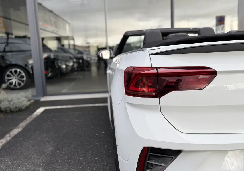 Vue 3/4 arrière droite d’un Volkswagen T-Roc Cabriolet blanc 2022 avec toit ouvert et feux arrière distinctifs R-Line.