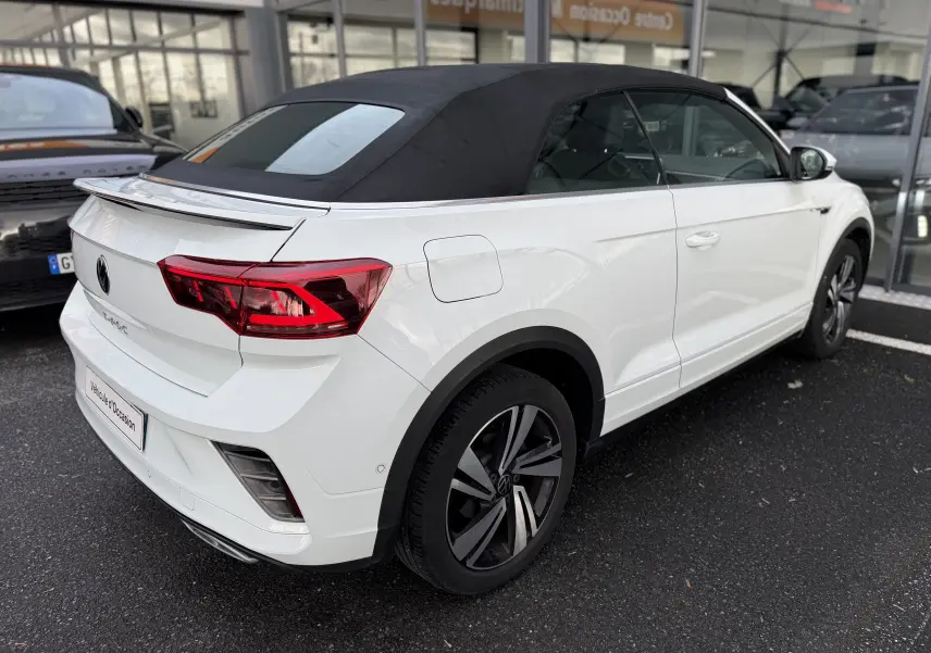 Vue 3/4 arrière droite d’un Volkswagen T-Roc Cabriolet blanc avec capote noire et jantes R-Line distinctives.