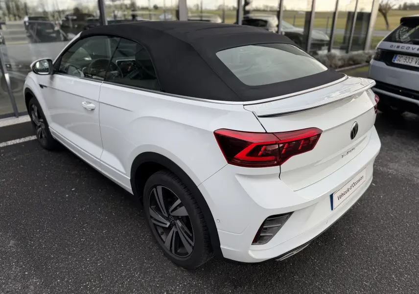Vue 3/4 arrière droite d’un Volkswagen T-Roc Cabriolet blanc 2022 avec toit souple noir et jantes R-Line.
