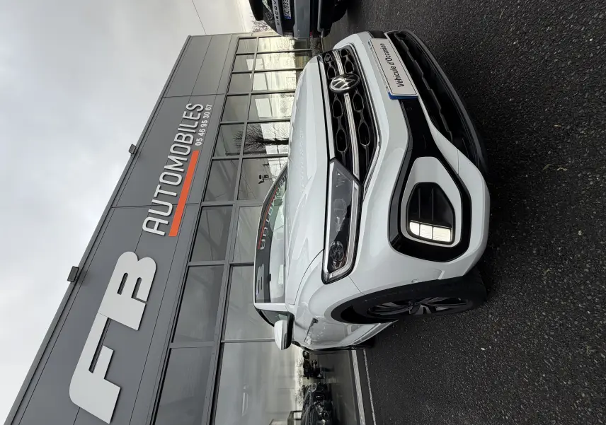 Vue 3/4 avant droit d'un Volkswagen T-Roc Cabriolet blanc 2022 avec finition R-Line devant un showroom.