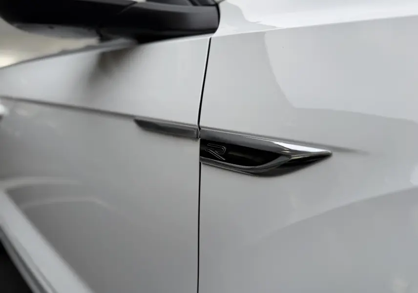 Détail du logo R noir sur la porte côté gauche d’un Volkswagen T-Roc Cabriolet blanc 2022 finition R-Line.