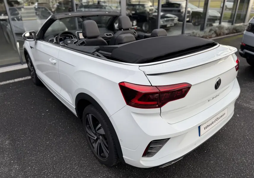 Vue 3/4 arrière droite du cabriolet Volkswagen T-Roc blanc avec toit souple noir partiellement ouvert et finition R-Line.
