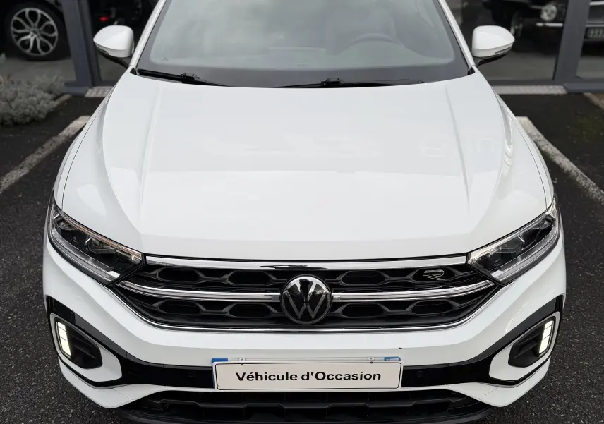 Vue frontale d'un Volkswagen T-Roc Cabriolet blanc avec capote noire, calandre chromée et phares allumés.