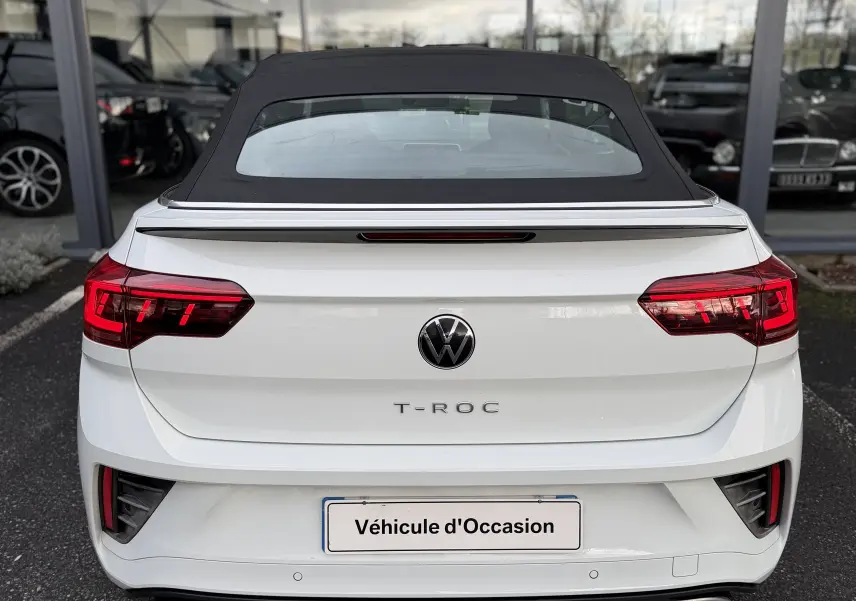 Vue arrière d’un Volkswagen T-Roc Cabriolet blanc 2022 avec toit noir fermé et feux arrière LED allumés.