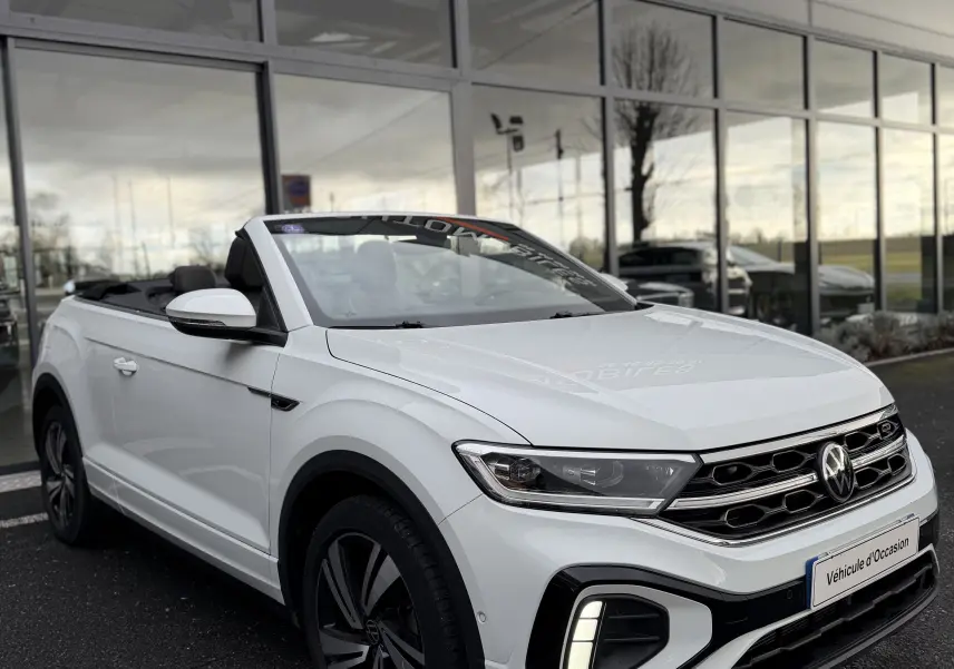 Volkswagen T-Roc Cabriolet blanc en 3/4 avant, capote ouverte, avec détails R-Line et feux LED allumés.