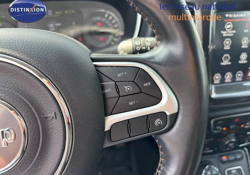 Gros plan sur le volant cuir noir du Jeep Compass 2021 avec commandes de régulateur de vitesse et tableau de bord flou.