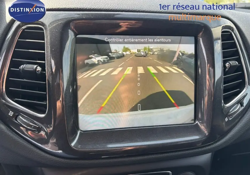 Écran central du Jeep Compass blanc montrant la caméra de recul avec lignes de guidage colorées.