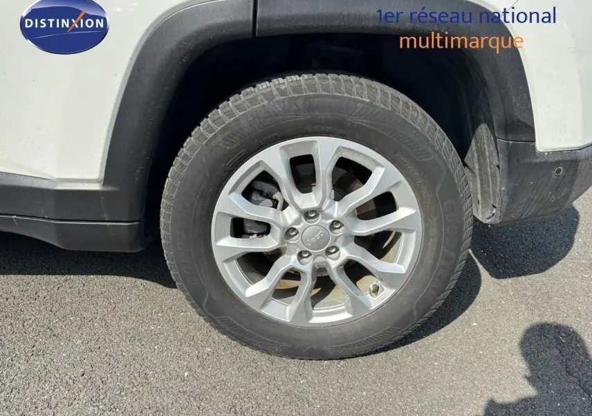 Gros plan sur la roue avant droite d’un Jeep Compass blanc, avec jante alliage argentée et pneu Goodyear.