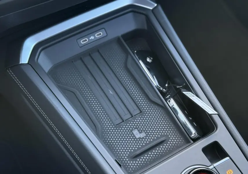 Gros plan sur la console centrale noire du Volkswagen T-Roc 2026 avec zone de charge sans fil et ports USB-C.