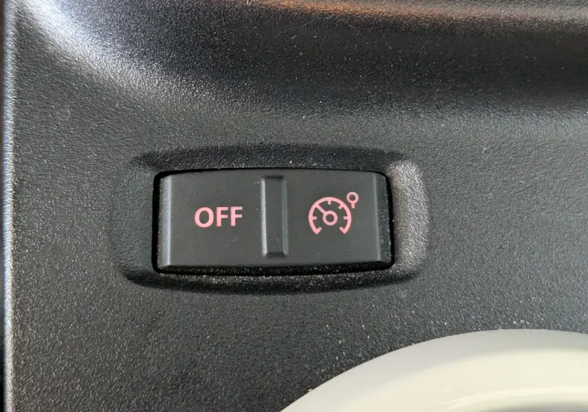 Gros plan sur le bouton noir du régulateur de vitesse avec indication "OFF" en rouge dans une Renault Twingo III noire.