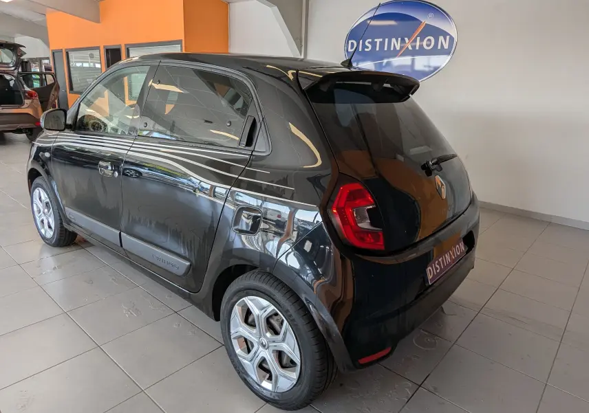 Vue 3/4 arrière droite d'une Renault Twingo III noire 2019 avec bandes blanches latérales et jantes argentées en showroom.