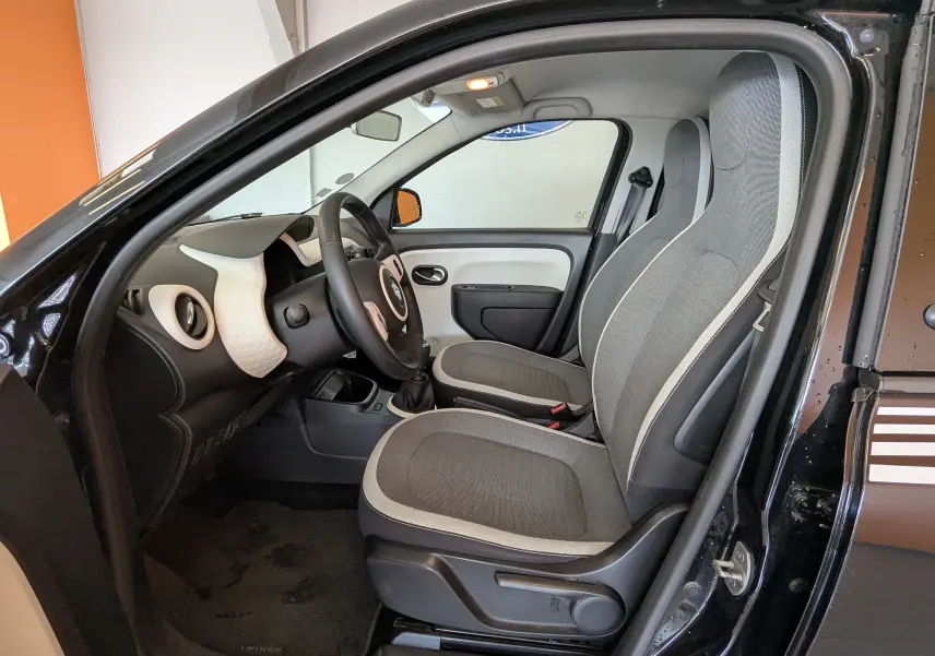 Vue intérieure côté conducteur de la Renault Twingo III noire, montrant les sièges gris et le tableau de bord clair.