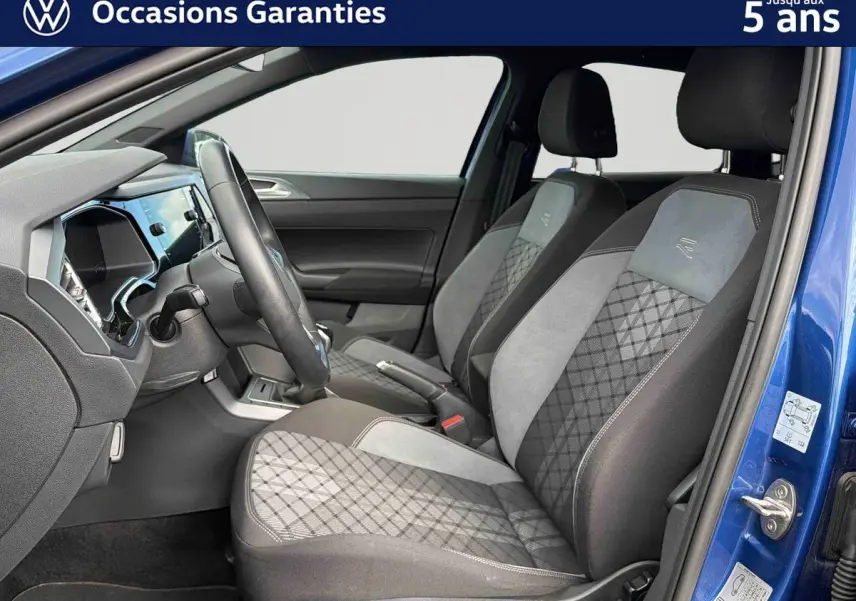 Vue intérieure côté conducteur de la Volkswagen Polo bleue 2025, sièges avant en tissu gris et noir avec surpiqûres contrastées.