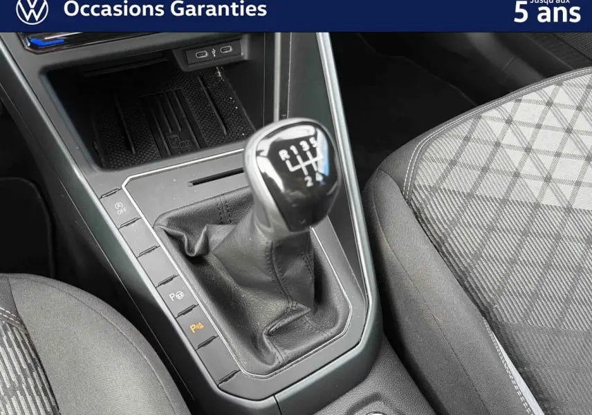 Le levier de vitesses manuel noir de la Volkswagen Polo 2025, avec console centrale et siège avant gris à motifs.