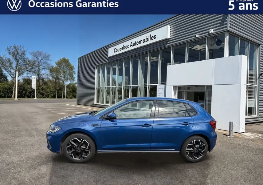Vue de profil côté gauche d'une Volkswagen Polo bleue métallisée stationnée devant un bâtiment moderne.