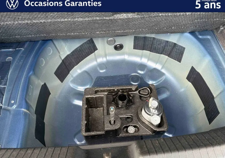 Vue plongeante sur le coffre ouvert d'une Volkswagen Polo bleue 2025, montrant la roue de secours et les outils.