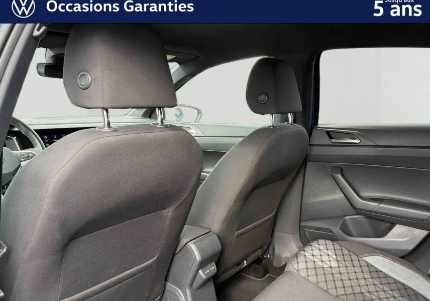 Vue intérieure arrière de la Volkswagen Polo 2025, sièges tissu gris foncé avec motifs et portières noires.