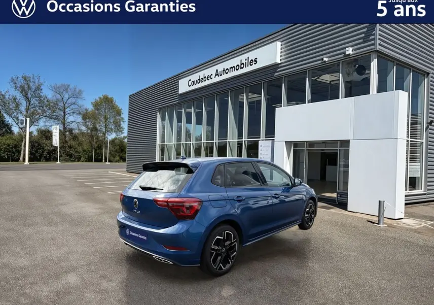 Volkswagen Polo bleue vue 3/4 arrière droit, avec toit noir et jantes alliage 17 pouces devant un concessionnaire.