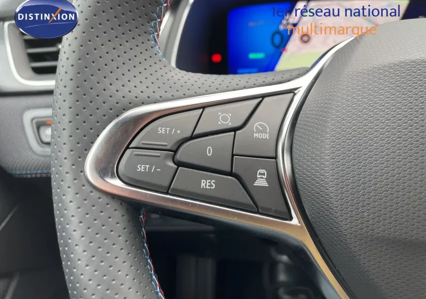 Gros plan sur les commandes à gauche du volant perforé du Renault Symbioz gris, avec affichage numérique en arrière-plan.