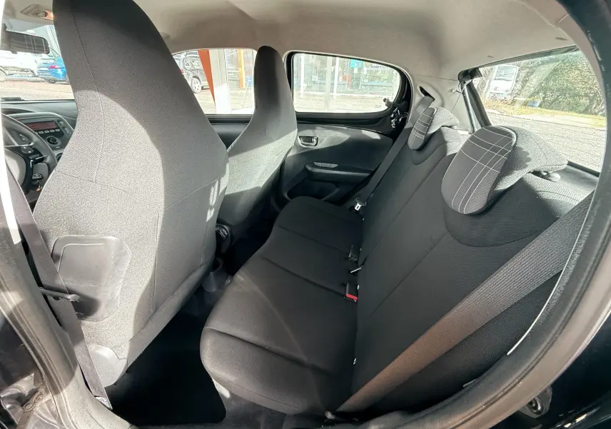 Vue intérieure arrière côté gauche du Peugeot 108 noir montrant les sièges en tissu gris foncé avec appuie-têtes à motifs rayés.