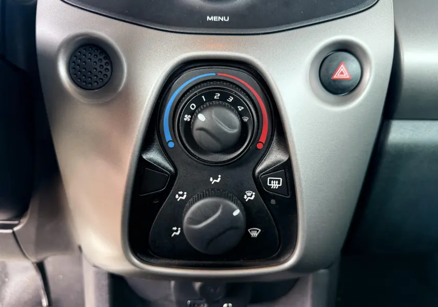 Gros plan sur les commandes de climatisation noires et grises du tableau de bord d'une Peugeot 108 noire de 2018.